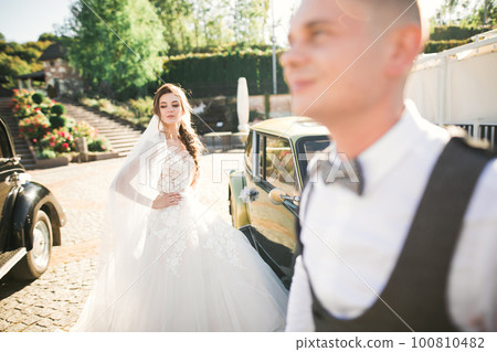 Wedding bride and groom, elegant couple staying near retro wedding car 100810482