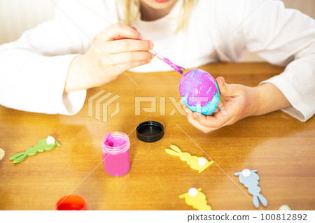Child hands painting eggs for Easter on the wooden table at home. Preparation for Easter celebration 100812892