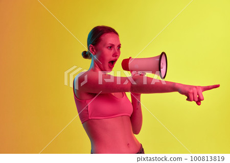 Expressive young girl shouting and screaming through loudspeaker over yellow-orange background in neon light. Sales, breaking news Expressive young girl shouting and screaming through loudspeaker over yellow-orange background in neon light. Sales, breaking news 100813819