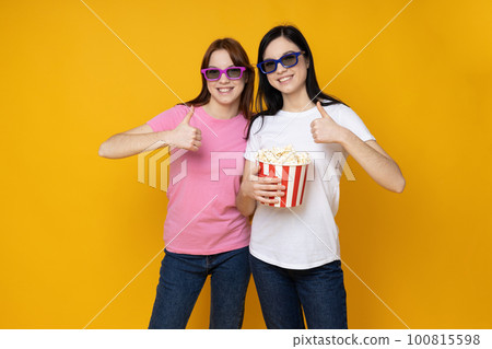 Two beautiful young women, sisters - twins on yellow background 100815598