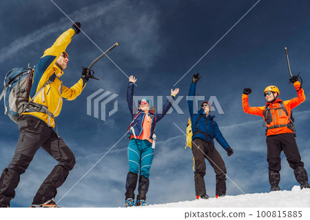 Low angle view, group of hikers jumping in the air when reaching the top of the snowy mountain 100815885