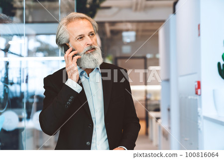 Portrait, waist up, senior business man in black suit talking on the phone, while at the office  100816064