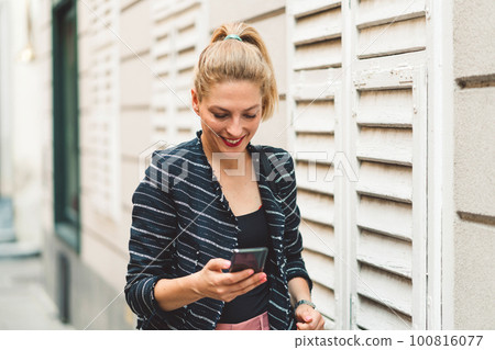 Woman running errands in the city, waist up looking at her phone while walking fast to a meeting  100816077