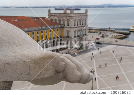 Lisbon, Portugal panoramic landscape defocused view of Commerce square, Praca do Comercio, with front ground focus on art detail marble leg on top of 1875 triumphal arch Arco da Rua Augusta. 100816083
