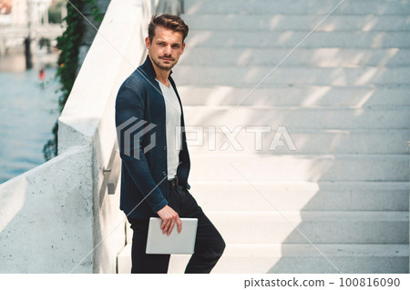 Side view of caucasian man standing on the stairs holding a tablet in one hand, sunny day outside Side view of caucasian man standing on the stairs holding a tablet in one hand, sunny day outside 100816090