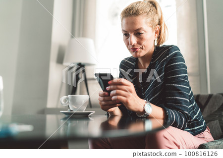 Young londe woman sitting at a cafe looking at her phone Young londe woman sitting at a cafe looking at her phone 100816126