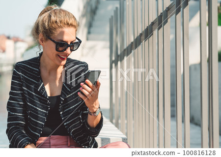 Woman with her hair in a ponytail looking at the phone while on a lunch break outside 100816128