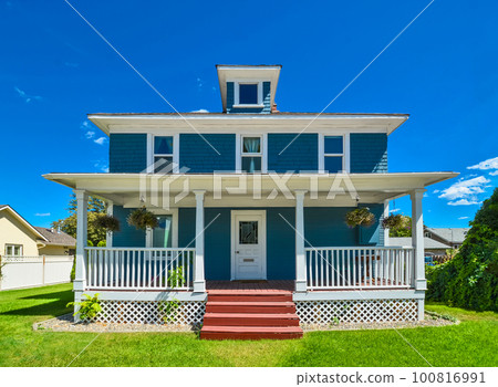 Historic family house with green lawn in front and blue sky background. 100816991