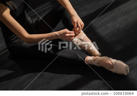 Faceless ballerina sits on the floor and puts on pointe shoes. Top view. Faceless ballerina sits on the floor and puts on pointe shoes. Top view. 100819064