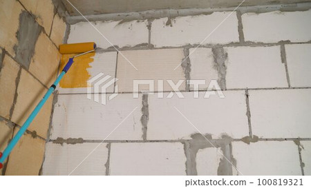 Colored primer for walls. Premises, manual stage of renovation work. Priming the wall with an orange roller. Applying an orange primer to the wall. Colored primer for walls. Premises, manual stage of renovation work. Priming the wall with an orange roller. Applying an orange primer to the wall. 100819321