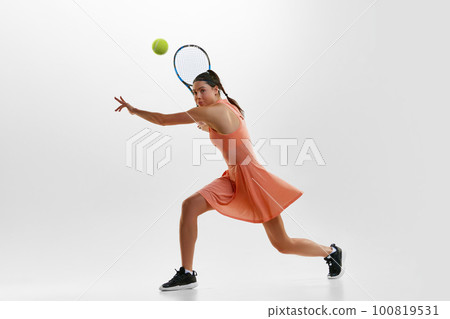 Portrait of young sportive, active woman, professional female tennis player training, hitting ball with racket against white studio background. 100819531