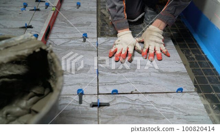 The worker holds a ceramic tile in his hand. The process of laying ceramic tiles in the bathroom. The worker holds a ceramic tile in his hand. The process of laying ceramic tiles in the bathroom. 100820414