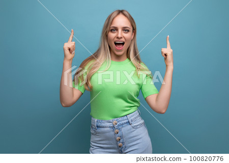 energetic girl in casual outfit screaming joyfully pointing up on blue background 100820776
