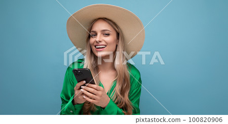 cute young woman on vacation in a summer straw hat with a phone on a blue studio background with 100820906