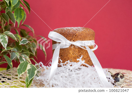 Sponge Easter cake with a white ribbon with quail eggs on a red background with a green plant. Sponge Easter cake with a white ribbon with quail eggs on a red background with a green plant. 100821047