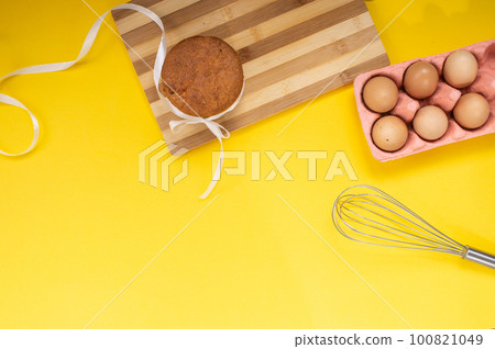 Easter pastries on the table with chicken eggs and a whisk on a yellow background. Top view 100821049
