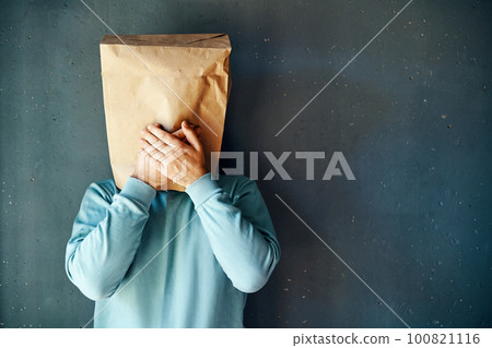Man with a paper bag on head covering mouth with hands over grey background 100821116