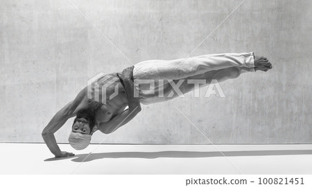 Black and white image, monochrome. Strong body. Muscular shirtless man practising yoga exercises against textured background 100821451