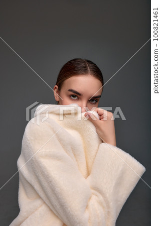 Beautiful fashionable woman in a cozy fur coat on a gray background positive girl posing at the camera in beautiful spring clothes Beautiful fashionable woman in a cozy fur coat on a gray background positive girl posing at the camera in beautiful spring clothes 100821461