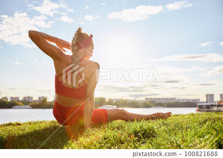 A woman is engaged in animal flow gymnastics outdoors near the river on green grass in red clothes. A woman is engaged in animal flow gymnastics outdoors near the river on green grass in red clothes. 100821688