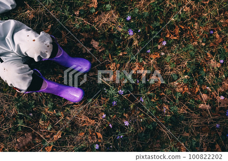 Unrecognizable little girl in violet boots and blue overall lying in spring blooming forest Unrecognizable little girl in violet boots and blue overall lying in spring blooming forest 100822202