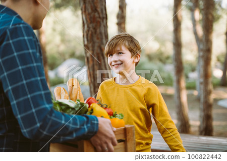 Father and son farmers holding a wooden crate with supplies groceries. Man male dad and his should kid boy child delivered a framed box with organic vegetables and bread to farmers market. Father and son farmers holding a wooden crate with supplies groceries. Man male dad and his should kid boy child delivered a framed box with organic vegetables and bread to farmers market. 100822442