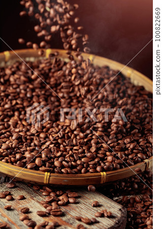 Medium-roasted coffee beans are poured into a basket. Medium-roasted coffee beans are poured into a basket. 100822669