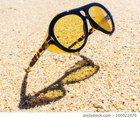 Unusual yellow sunglasses stuck in the sand on the beach 100822876