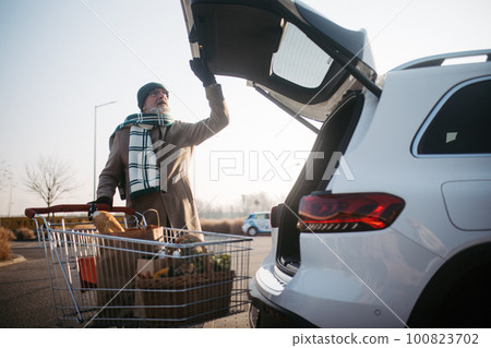 Senior man giving his purchase in electric car trunk. Senior man giving his purchase in electric car trunk. 100823702