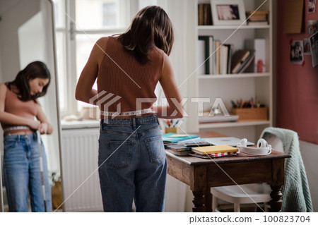 Young teenage girl looking in the mirror in her room. 100823704