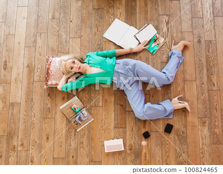 Fashionable woman reading fashion magazine while lying on the floor on pillow Fashionable woman reading fashion magazine while lying on the floor on pillow 100824465