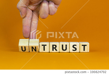 Untrust or trust symbol. Businessman turns wooden cubes, changes words 'untrust' to 'trust'. Beautiful orange table, orange background. Business and untrust or trust concept, copy space. Untrust or trust symbol. Businessman turns wooden cubes, changes words 'untrust' to 'trust'. Beautiful orange table, orange background. Business and untrust or trust concept, copy space. 100824702