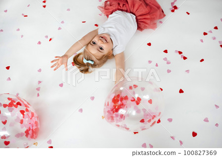 Little 2 years old girl playing with balloon with heart shape papers inside it and around  100827369