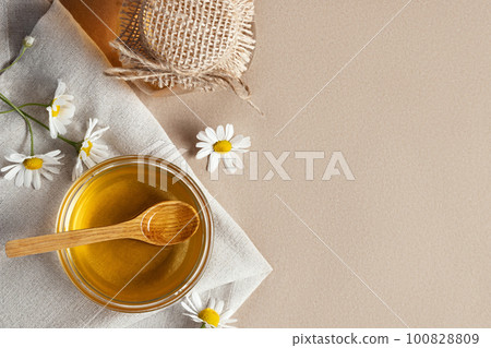 Chamomile syrup in a small bowl and in a jar and chamomile flowers on a linen kitchen towel, topview, copy space Chamomile syrup in a small bowl and in a jar and chamomile flowers on a linen kitchen towel, topview, copy space 100828809
