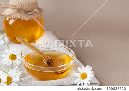 Chamomile syrup in a small bowl and in a jar and chamomile flowers on a linen kitchen towel, copy space Chamomile syrup in a small bowl and in a jar and chamomile flowers on a linen kitchen towel, copy space 100828810