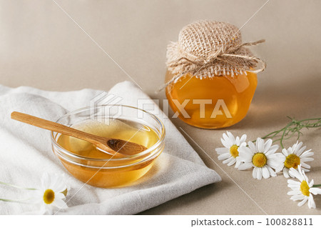 Chamomile syrup in a small bowl and in a jar and chamomile flowers on a linen kitchen towel 100828811