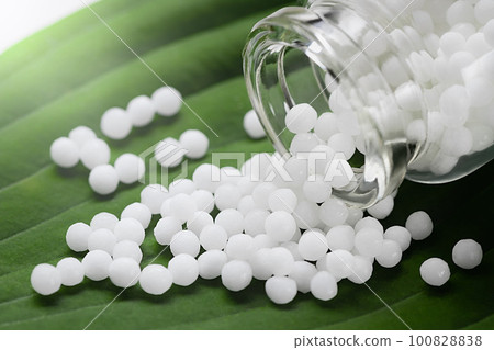 Homeopathic pills scattered from a bottle on a green leaf, close up Homeopathic pills scattered from a bottle on a green leaf, close up 100828838