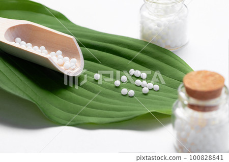 Homeopathic pills scattered from a wooden scoop on a green leaf Homeopathic pills scattered from a wooden scoop on a green leaf 100828841