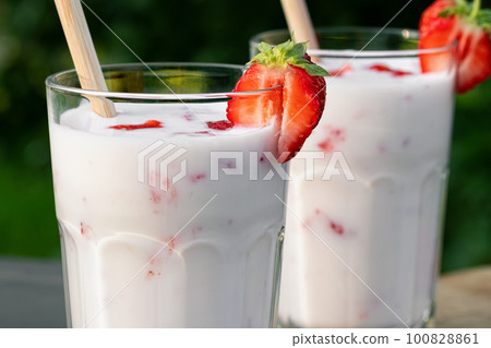 Strawberry smoothie in two glass glasses and fresh strawberries on a wooden table in the yard, close up Strawberry smoothie in two glass glasses and fresh strawberries on a wooden table in the yard, close up 100828861