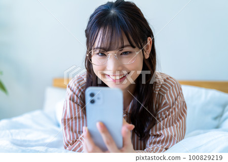 Young woman in pajamas using smartphone in bed 100829219