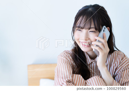 穿著睡衣的年輕女人用智能手機打電話 穿著睡衣的年輕女人用智能手機打電話 100829560
