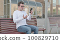 Young Man Reacting to Loss on Smartphone while Sitting Outdoor on Bench 100829710