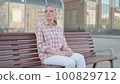 Outdoor Young Man Checking Time while Waiting on Bench 100829712