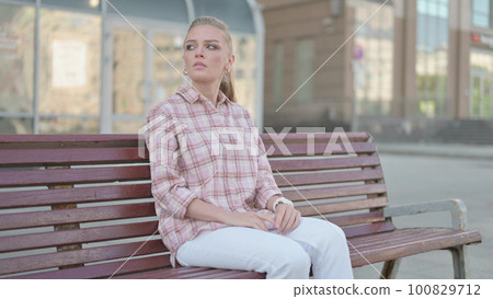 Outdoor Young Man Checking Time while Waiting on Bench 100829712