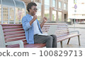 Young African Man Celebrating Success on Laptop while Sitting Outdoor on Bench 100829713