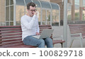 Coughing Young Man Using Laptop while Sitting Outdoor on Bench 100829718