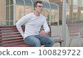 Young Man having Back Pain while Sitting on Bench Outdoor 100829722