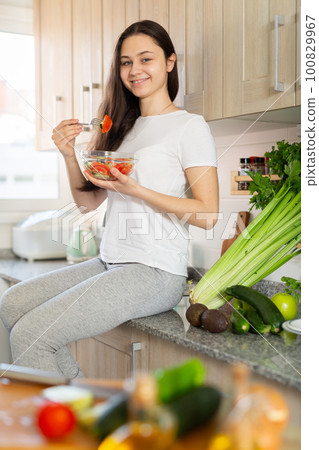 Woman eating vegetable salad at home kitchen 100829967