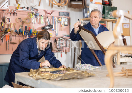 collected male restorer carefully covers carved wooden frame of antique mirror with layer of varnish 100830013