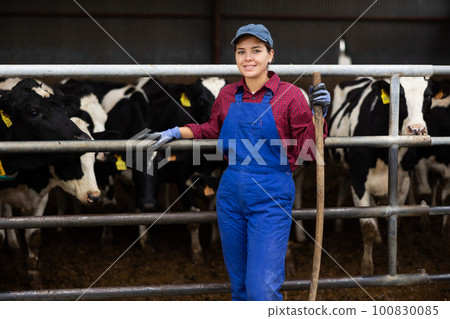 Portrait of smiling European female farmer in uniform with rake during work on dairy farm 100830085